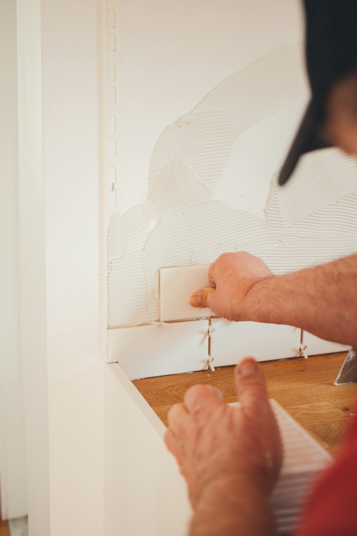 A mature Caucasian man in uniform squats and writes a note on a piece of paper on the floor before replacing an old window frame with a new one in a bedroom on a sunny spring day. Vertical side view, medium shot. Concept: repair and replacement of windows and window frames, using technology, mathematical calculations.